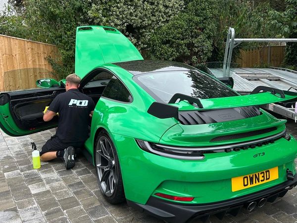 A man detailing a bright green Porsche GT3 with open doors and hood.