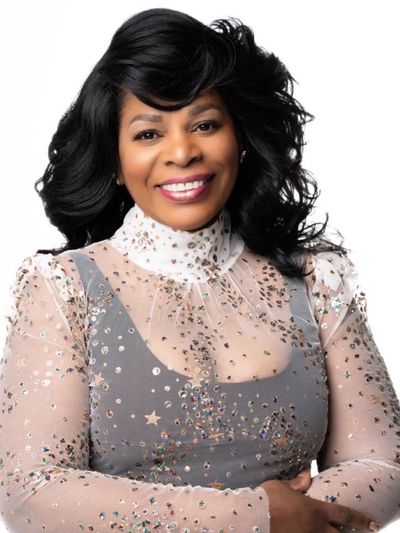 Smiling woman in a sparkling, sheer top with voluminous hair.