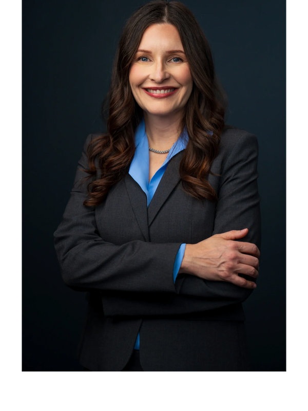 Confident woman in a dark suit with curly hair smiling.