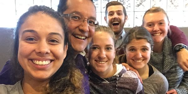 Group selfie of six happy people indoors.