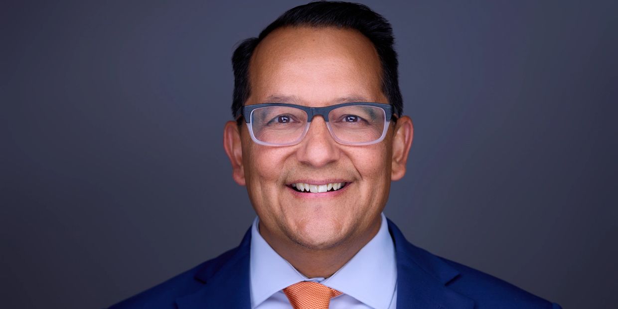 Smiling man in suit and glasses against a plain background.