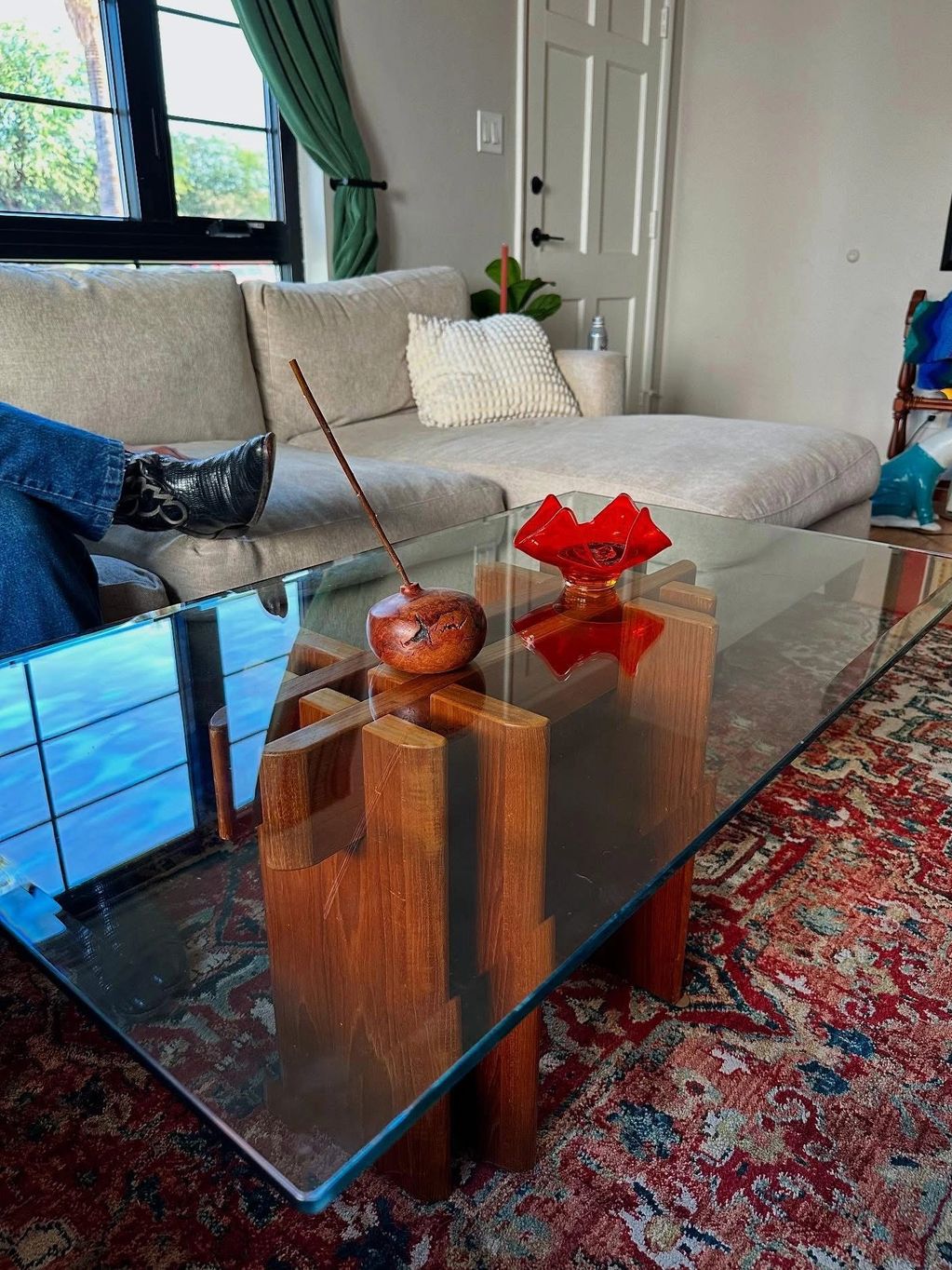 Modern glass coffee table with wooden base and decorative items in a cozy living room.