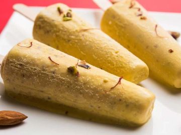 Three creamy mango kulfis garnished with saffron and pistachios on a white plate.