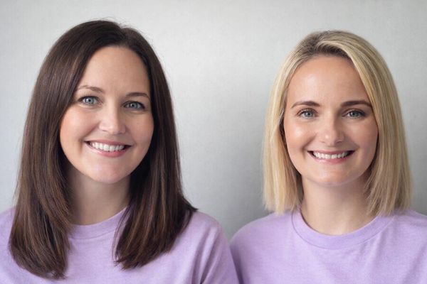 Two smiling women with different hair colors wearing matching lavender tops.