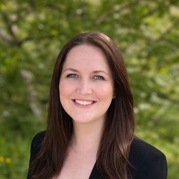 Smiling woman with brown hair outdoors in a black blazer.
