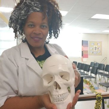 Woman in lab coat holding a human skull model in a classroom.