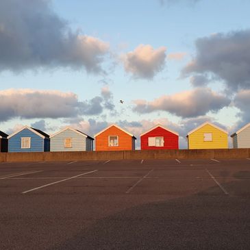 Colorful beach huts under a cloudy sky at sunset.