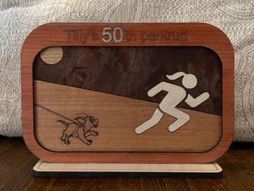 Wooden plaque celebrating Tilly's 50th parkrun with running figure and dog.