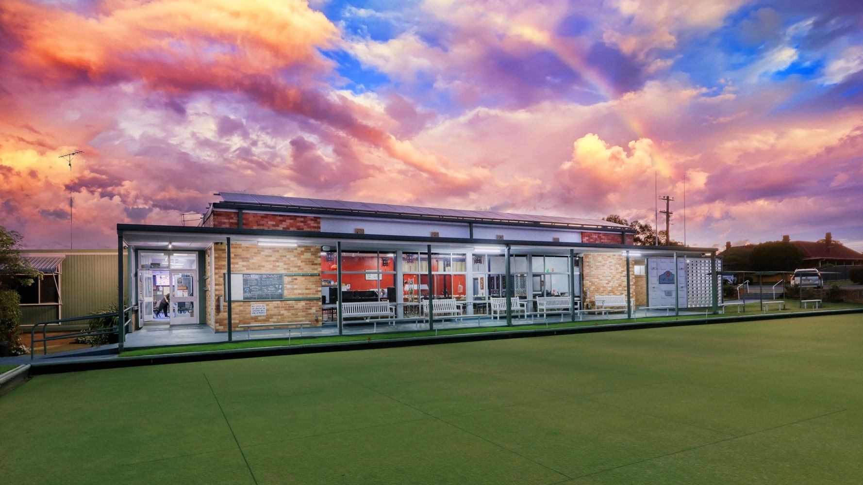 A bowling club building under a colorful sunset sky with a faint rainbow.