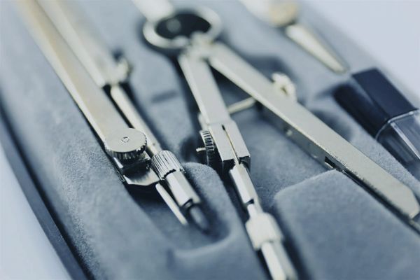 Close-up of metal drafting compasses in a gray case.
