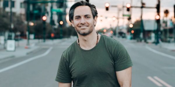 A man smiling confidently on a city street during sunset.