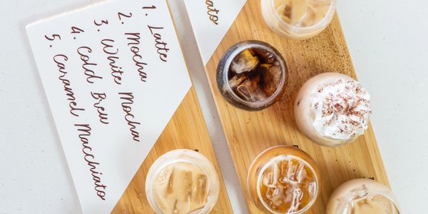 A wooden tray with six iced coffee drinks and a handwritten coffee menu.