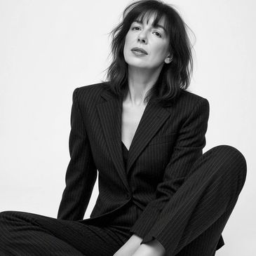 Woman in a pinstripe suit posing confidently against white background.
