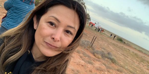 Jacqui in the Woomera desert with helicopter in background with Hayabusa2 sample return capsule