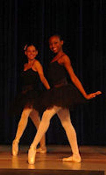 Two young ballerinas performing on stage in black tutus.
