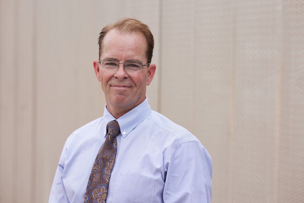 Middle-aged man in glasses and a tie smiling gently at the camera.