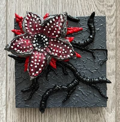 A dark, textured artwork featuring a red and black flower with white teeth and tentacle-like roots