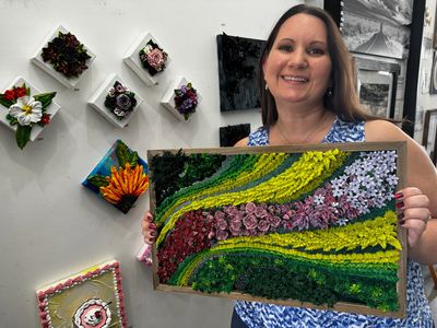 Tina holding vibrant artwork featuring cascading lines of green, yellow, pink, and blue flowers