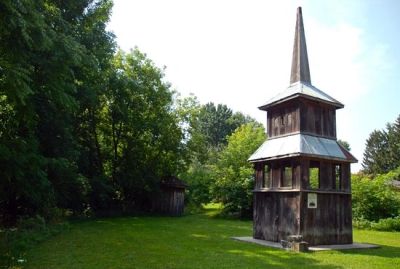 Wooden bell tower structure in a green park with trees.