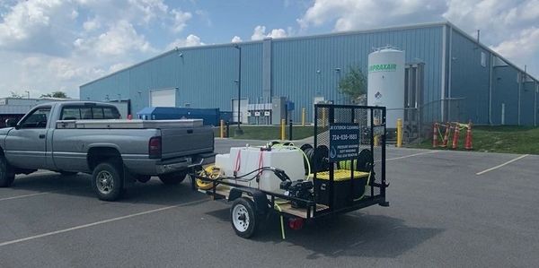Pickup truck towing a trailer with equipment in an industrial parking lot.