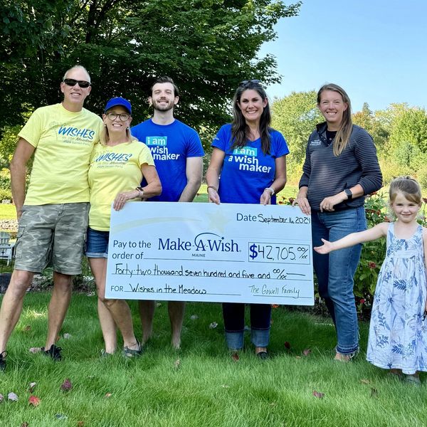 Group holding a large $42,705 Make-A-Wish donation check outdoors.
