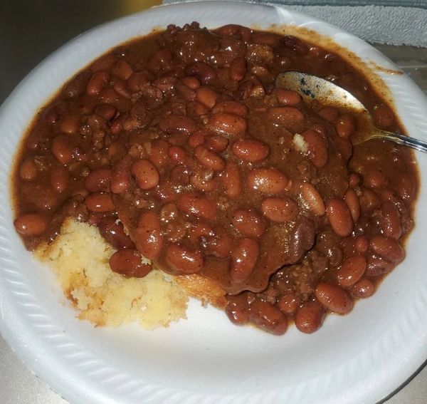 Plate of chili with beans and cornbread on a white disposable plate.