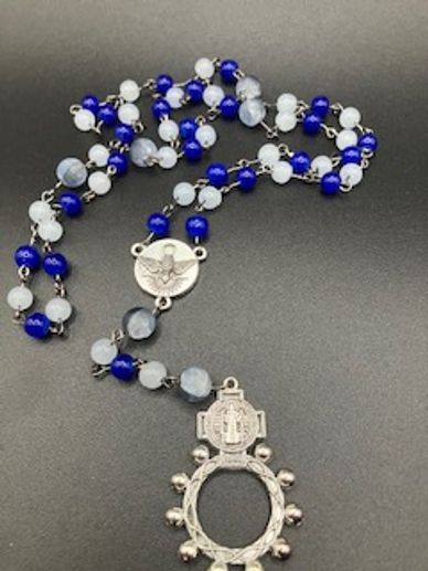 A blue and white beaded rosary with silver medallions on a black background.