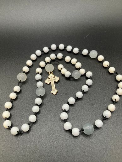 White bead rosary necklace with a gold cross on a black background.