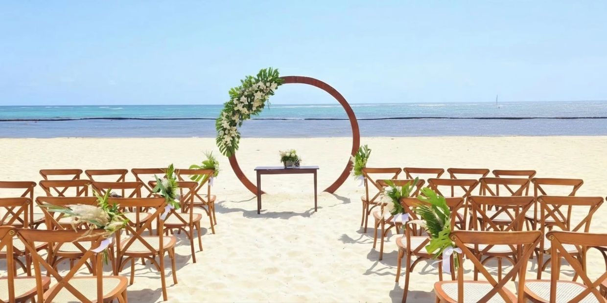 Beach wedding setup with wooden chairs and floral decorations.