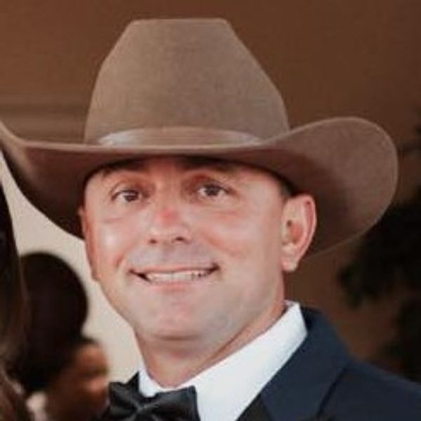 Man in tuxedo and cowboy hat smiling at an event.