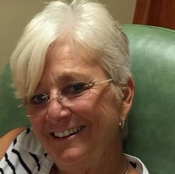 Smiling woman with short white hair and glasses in a striped top.