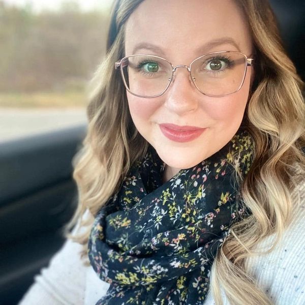 Woman with glasses and floral scarf smiling inside a car.
