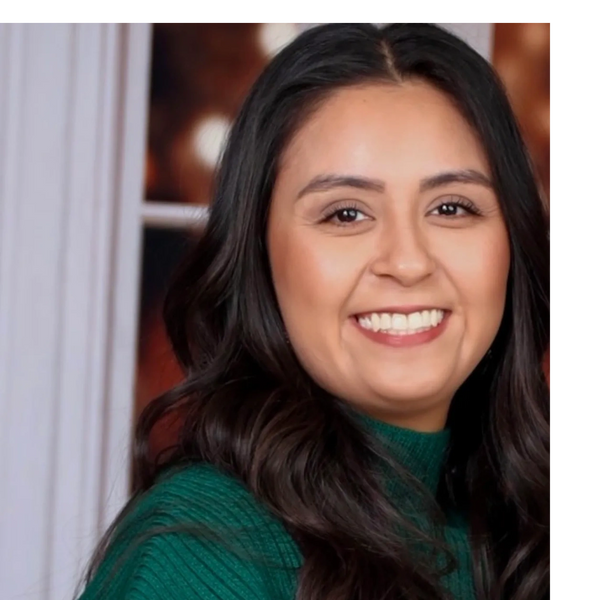 Smiling woman with long dark hair wearing a green knitted top.