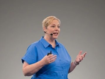 Woman in blue shirt speaking with a headset microphone.
