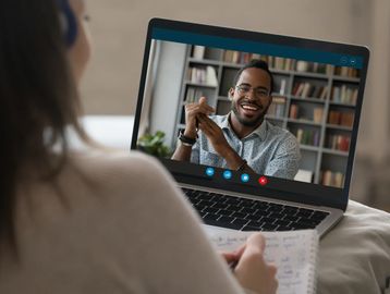 A woman video calls a smiling man while taking notes.