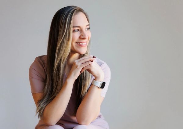 Smiling woman with long hair wearing a smartwatch, looking thoughtfully to the side.