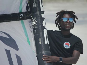 Man holding a windsurfing sail, wearing sunglasses and a black t-shirt.