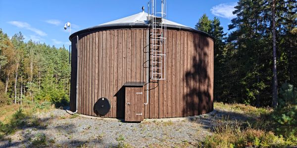 Large round wooden water tank with a metal ladder outdoors.