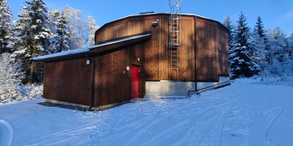 Wooden building with a red door in snowy landscape under clear blue sky.
