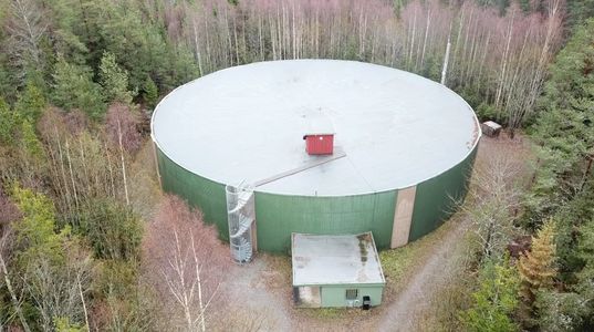 Large circular green water tank surrounded by trees in a forest area.