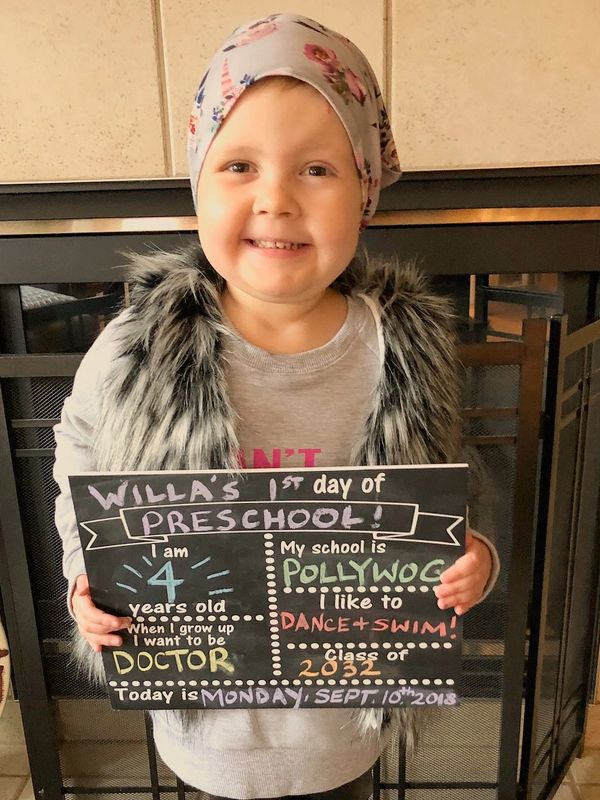 Smiling girl holding a chalkboard on her first day of preschool.