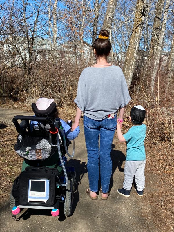 Woman holding hands with two children, one in a wheelchair, on a path.