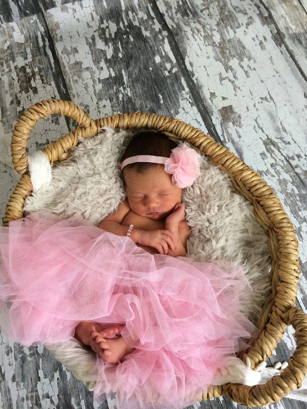 Newborn baby girl sleeping in a basket with pink dress and flower headband.
