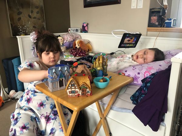 Child playing with toys next to a sick child in bed.