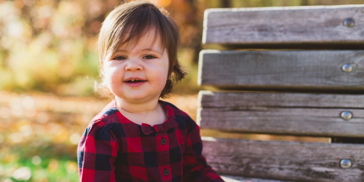 Toddler smiling on a wooden bench outdoors.
