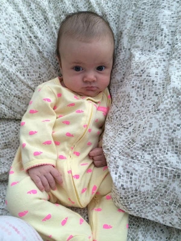 Baby in a yellow onesie lying on a patterned blanket.