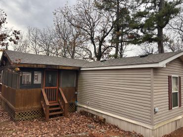 A beige mobile home with a screened porch surrounded by leafless trees.