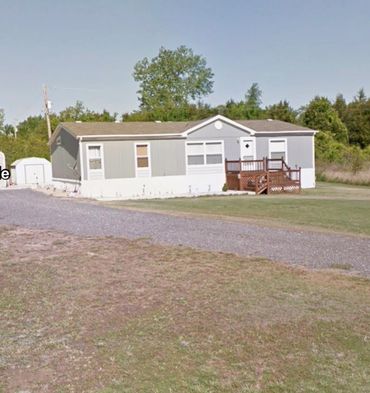 Single-story mobile home with a small porch and gravel driveway.