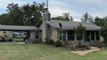 Single-story stone house with a large lawn and carport.