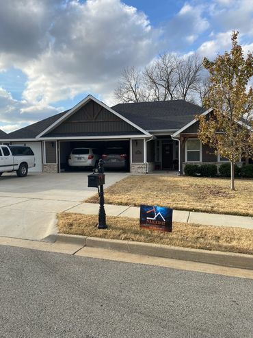 Suburban house with a driveway, parked cars, and a lawn sign.